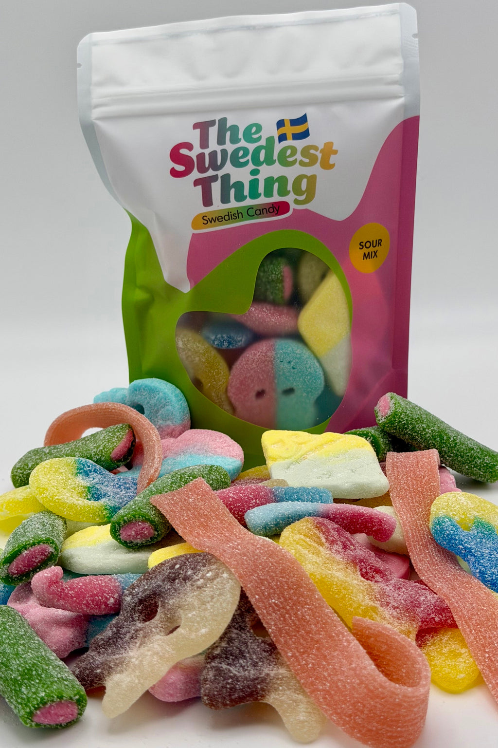 Colorful gummy candies spilling out of a 'The Swedest Thing' bag on a white background